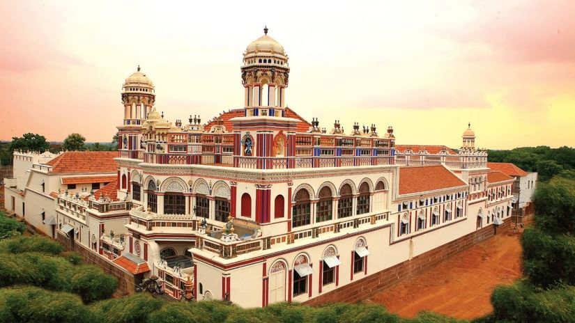 Facade view of Chidambara Vilas-Luxury Chettinad Heritage Resort, surrounded by greenery and pink skies. 