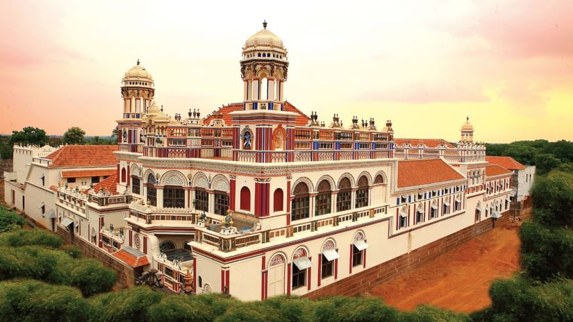 Facade view of Chidambara Vilas-Luxury Chettinad Heritage Resort, surrounded by greenery and pink skies. 