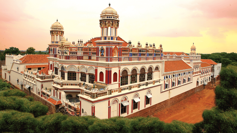 Facade view of Chidambara Vilas - A Luxury Chettinad Heritage Resort, surrounded by greenery and pink skies. 