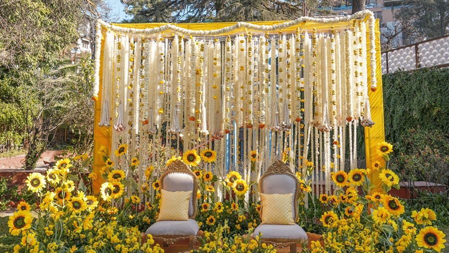 An outdoor wedding setup with yellow flower decorations, a golden drape backdrop, and 2 chairs at Ramada by Wyndham Mussoorie Mall Road.
