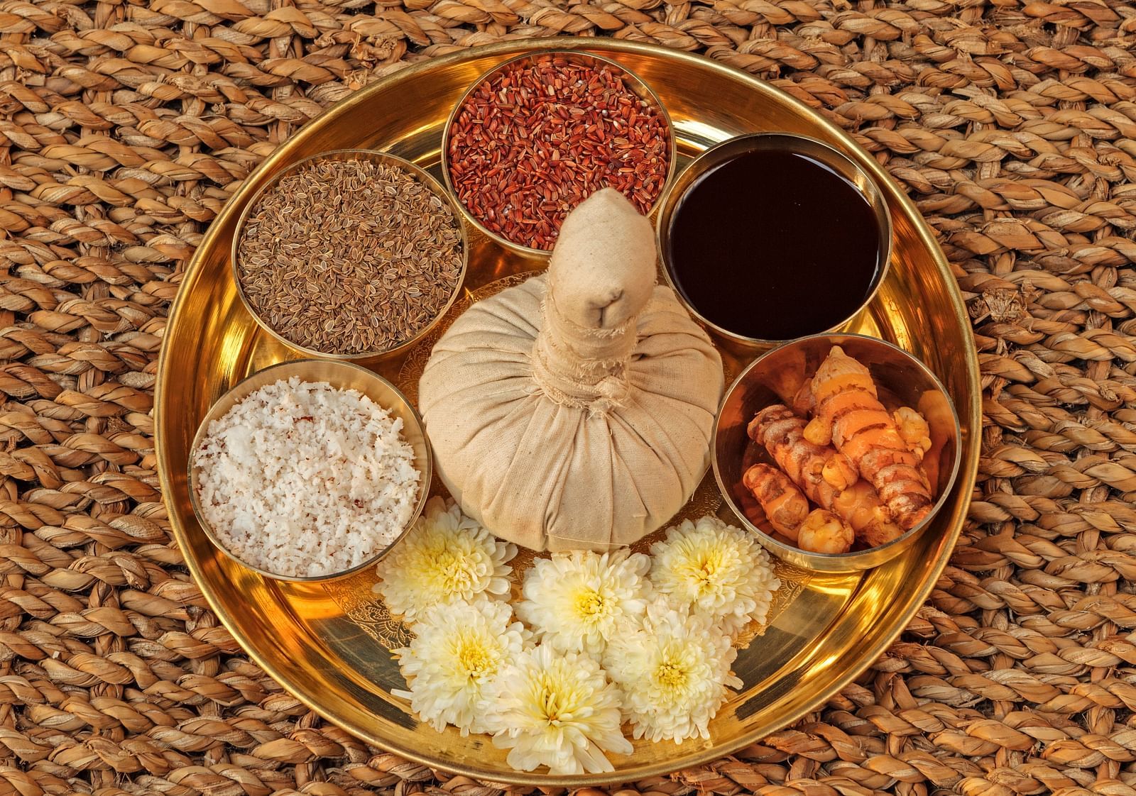 A golden tray with small bowls containing various ingredients, arranged on a woven surface.