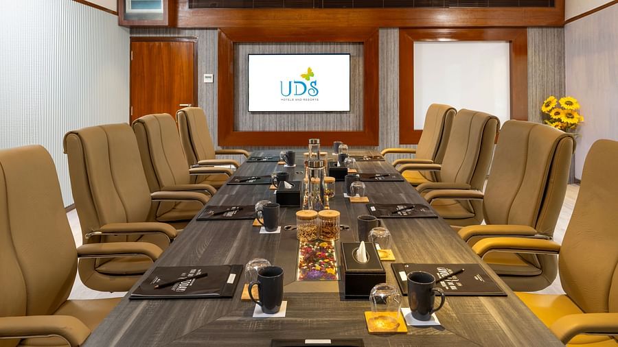 An image of a boardroom with chairs arranged around a table, with a mug, notepad, pen, and water glass placed on the table, and a presentation screen at the front - Uday Samudra Leisure Beach Hotel