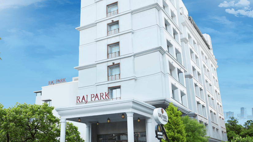 The facade of Raj Park Hotel, Chennai surrounded by greenery, with a bright sky in the background - Raj Park Hotel, Chennai