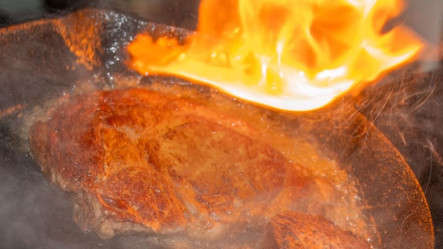 Steak being flambéed in a hot skillet with open flames in the kitchen at Narrow Gauge Inn.