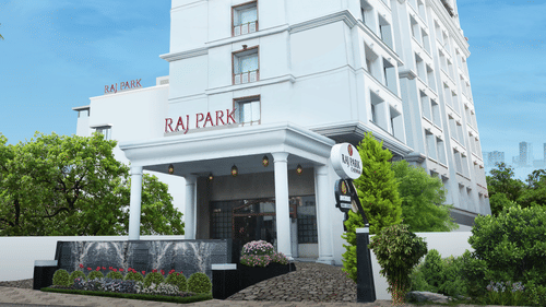The facade of Raj Park Hotel, Chennai surrounded by greenery, with a bright sky in the background - Raj Park Hotel, Chennai