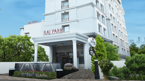 The facade of Raj Park Hotel, Chennai surrounded by greenery, with a bright sky in the background - Raj Park Hotel, Chennai