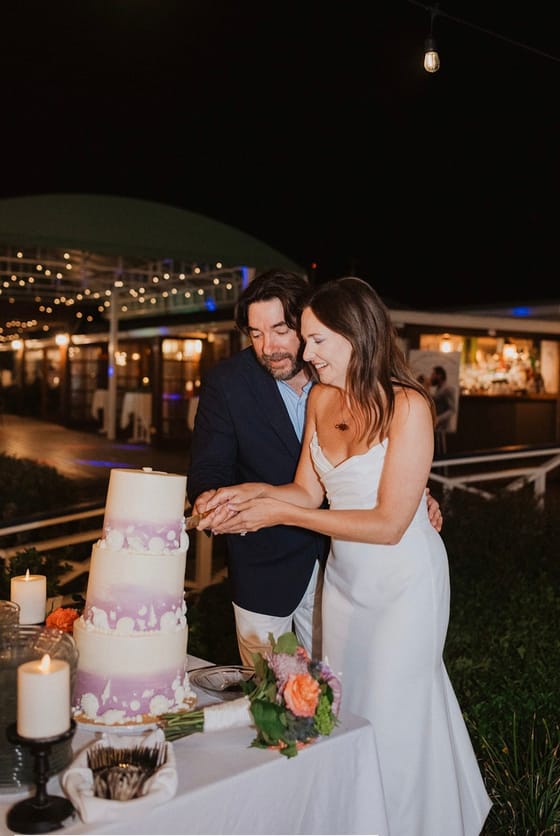 Newlyweds cutting their wedding cake by string lights at Abaco Inn