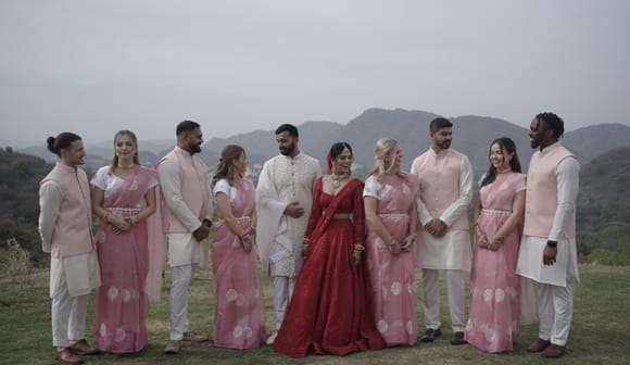 Bride in red and groom in cream with their party in pink saris and cream sherwanis on a hilltop lawn, Aravalli hills behind, at Fateh Vilas, Udaipur.