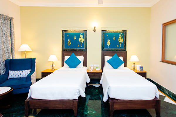 Deluxe Room: twin beds with blue cushions, blue armchair and green marble floor in a guest room