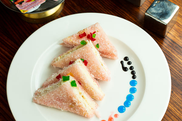 Food: pink coconut-coated sandwich triangles on a white plate with colourful sauce dots