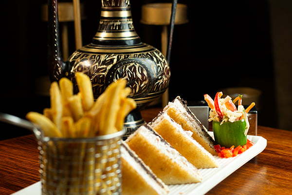 Food: club-style sandwich triangles with french fries in a wire basket beside a brass vase