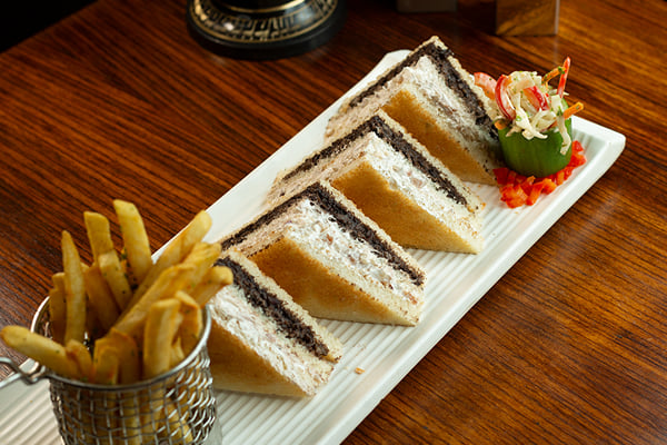 Food: sandwich slices with dark filling on a rectangular plate beside fries in a basket