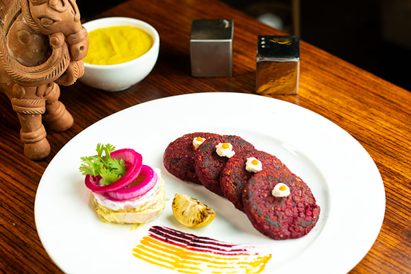 Food: round beetroot patties with cream dots, lemon half and pickled onion on a white plate
