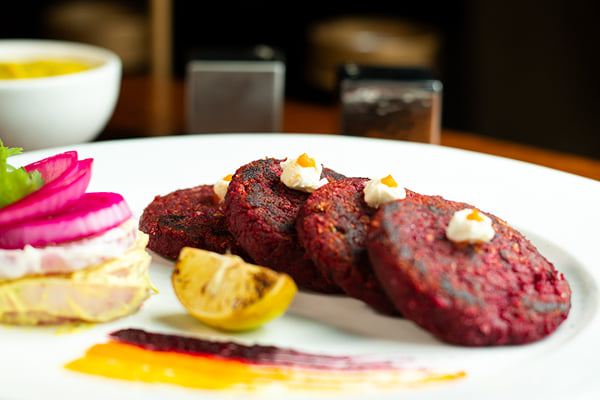 Food: close-up of beetroot patties with cream dots and a lemon half on a plate