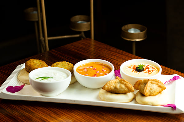 Food: rectangular platter of fritters, samosa-like pastries and three dips in white bowls