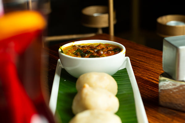 Food: three steamed rice cakes on banana leaf with a bowl of lentil curry