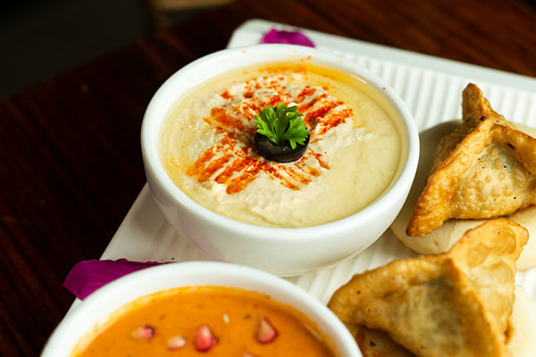 Food: close view of hummus-style dip, orange pomegranate dip and fried pastries on a platter