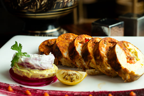 Food: sliced stuffed chicken roll with beetroot sauce streak, lemon half and garnished stack