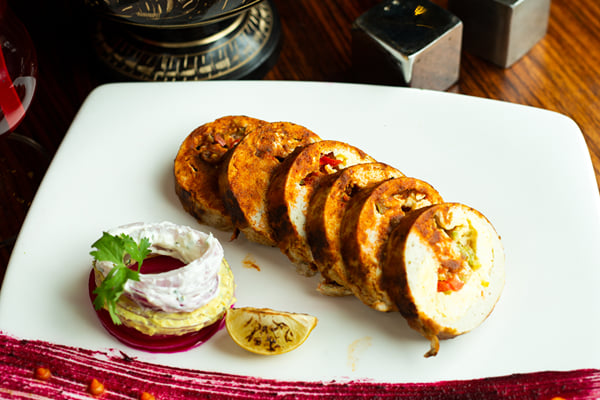 Food: sliced stuffed roll on a square plate with beetroot sauce and a garnished stack