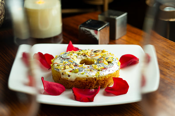 Food: ring-shaped dessert topped with silver leaf and nuts, surrounded by red rose petals