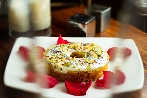 Food: close view of ring-shaped nut-topped dessert with rose petals and a candle behind