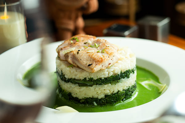 Food: stacked rice and spinach layers topped with grilled fish in green sauce