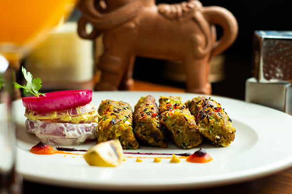 Food: green kebab pieces on a plate with garnished stack, orange drink and terracotta horse