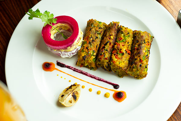Food: overhead view of four green kebabs, garnished ring and lemon half on a white plate