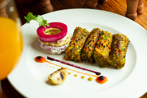 Food: angled view of four green kebabs on a plate with terracotta horses and orange drink