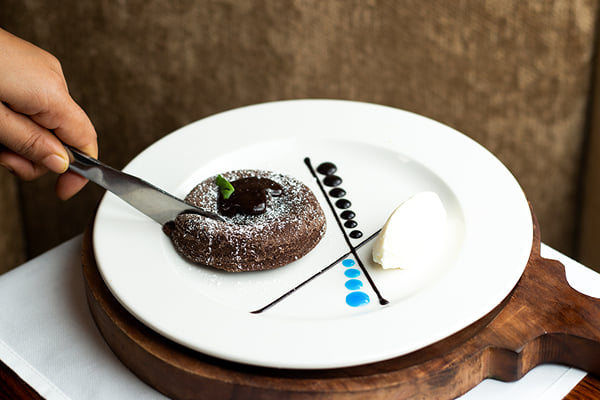 Food: hand cutting a chocolate lava cake with a knife, ice cream on the side