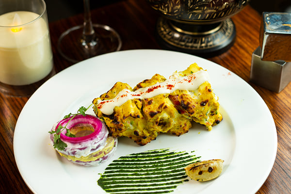 Food: tikka pieces drizzled with cream, with pickled onion stack and green chutney streak