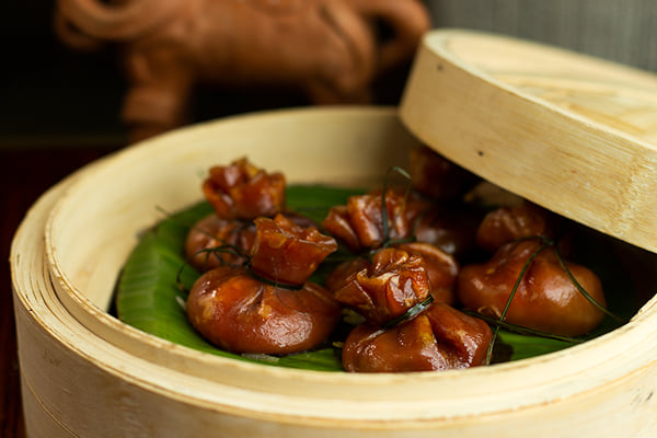 Food: wrapped brown dumplings in a bamboo steamer on banana leaf with partly open lid