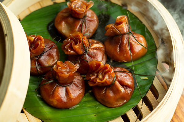 Food: brown pouch-shaped dumplings in an open bamboo steamer with visible steam