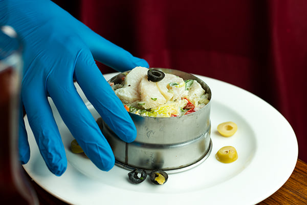 Food: gloved hand holding a metal ring mould of creamy salad on a white plate