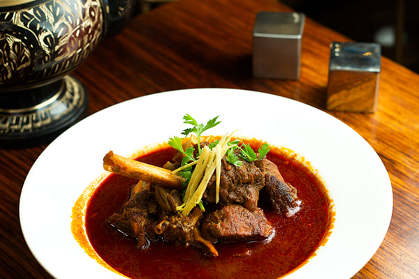 Food: mutton curry with bone, ginger strips and coriander in a white bowl