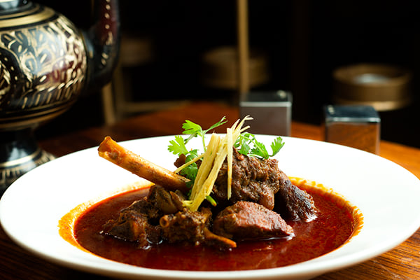 Food: close view of mutton curry with bone, ginger strips and herbs in a white bowl