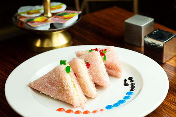 Food: pink coconut-coated sandwich triangles on a plate with a tiered stand of jam sachets