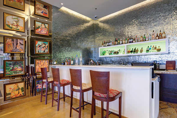 Liquid Lounge: bar counter with stools, backlit bottle display and wall of framed paintings