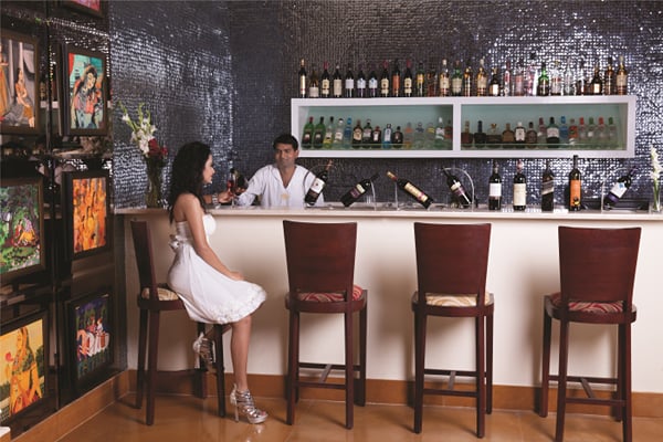 Liquid Lounge: woman in white dress seated at bar counter with bartender behind and bottle shelves