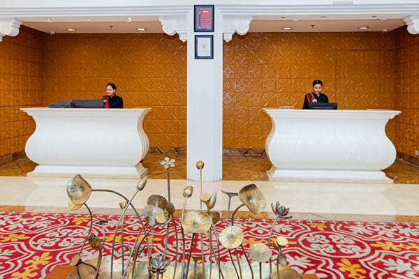 Lobby: two white reception desks with staff behind and metal lotus sculpture in foreground