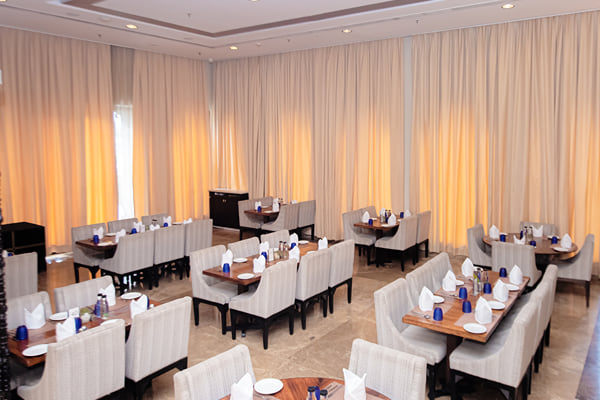 Myra restaurant: restaurant dining area with set tables, upholstered chairs and gold curtains