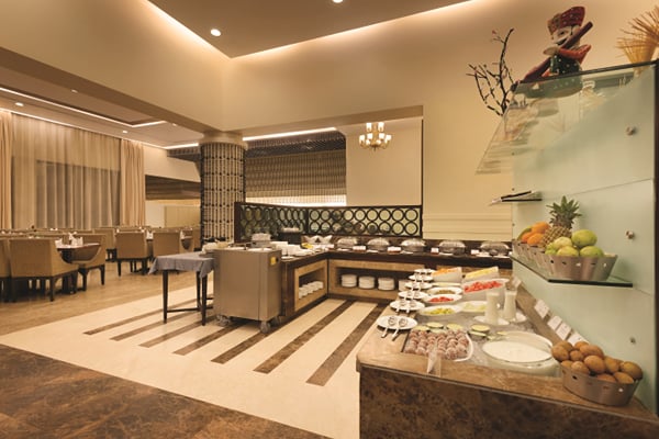 Myra restaurant: buffet station with fruit display, dining area with chairs and chandelier behind