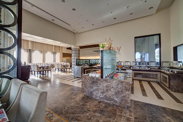 Myra restaurant: restaurant with marble buffet counter, dining tables in background and lounge chairs at left