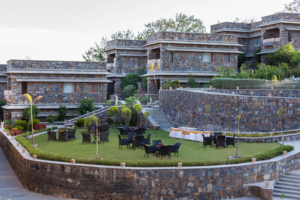 Gardens: terraced lawn with black wicker seating and a draped table, stone buildings behind