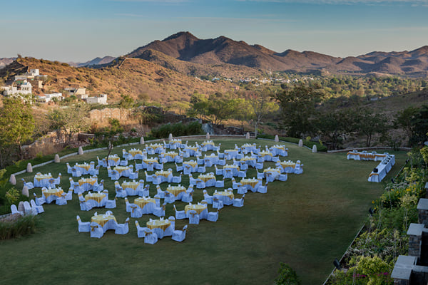 Outdoor venue: lawn set with many round tables and chair covers, hills in the background