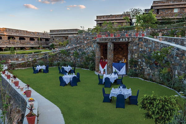 Outdoor venue: lawn set with dining tables and navy chairs near a stone alcove with decorated stage