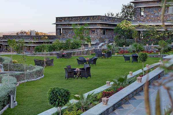 Gardens: green lawn with wicker chairs and tables, stone buildings and shrubs around