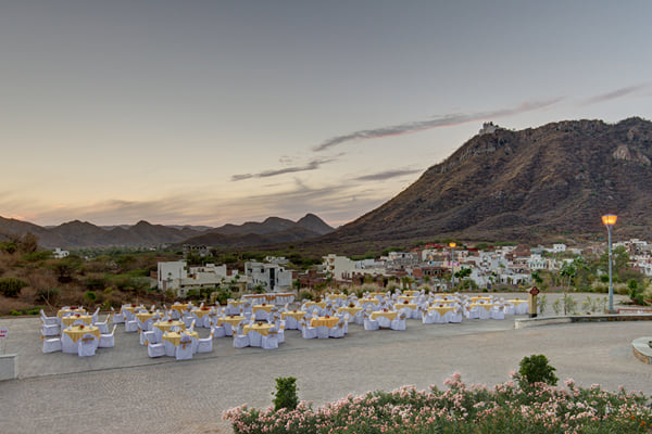 Outdoor venue: open terrace set with many round tables and chair covers at dusk, hills behind