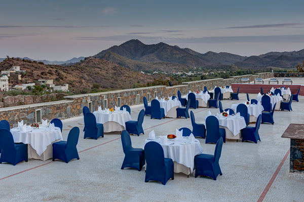 Outdoor venue: terrace with white-clothed round tables and navy chair covers, hills in the distance