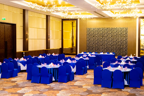 Panghat hall: banquet hall with round tables, blue chair covers and chandeliers under a decorated ceiling